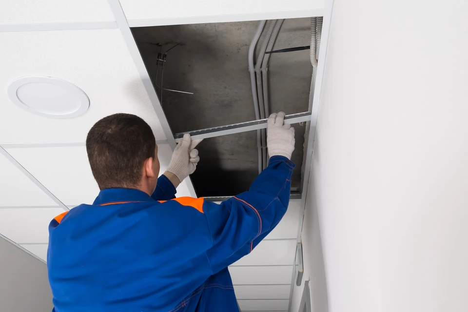Un homme effectue des travaux de finition au plafond dans un intérieur moderne avec mobilier blanc