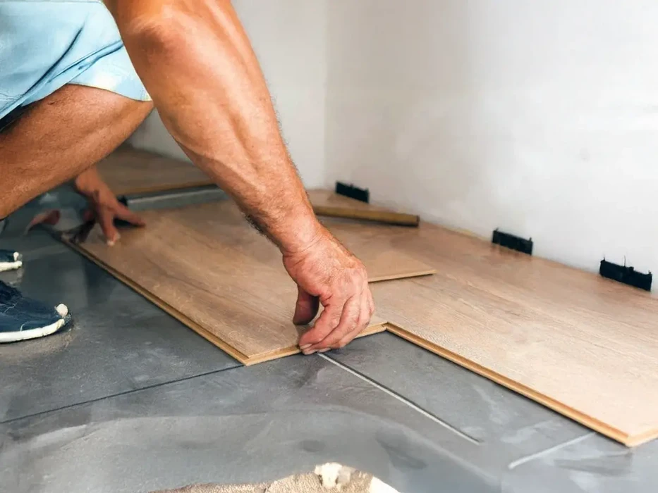 Deux hommes agenouillés installent un parquet en bois massif dans une pièce aux murs blancs