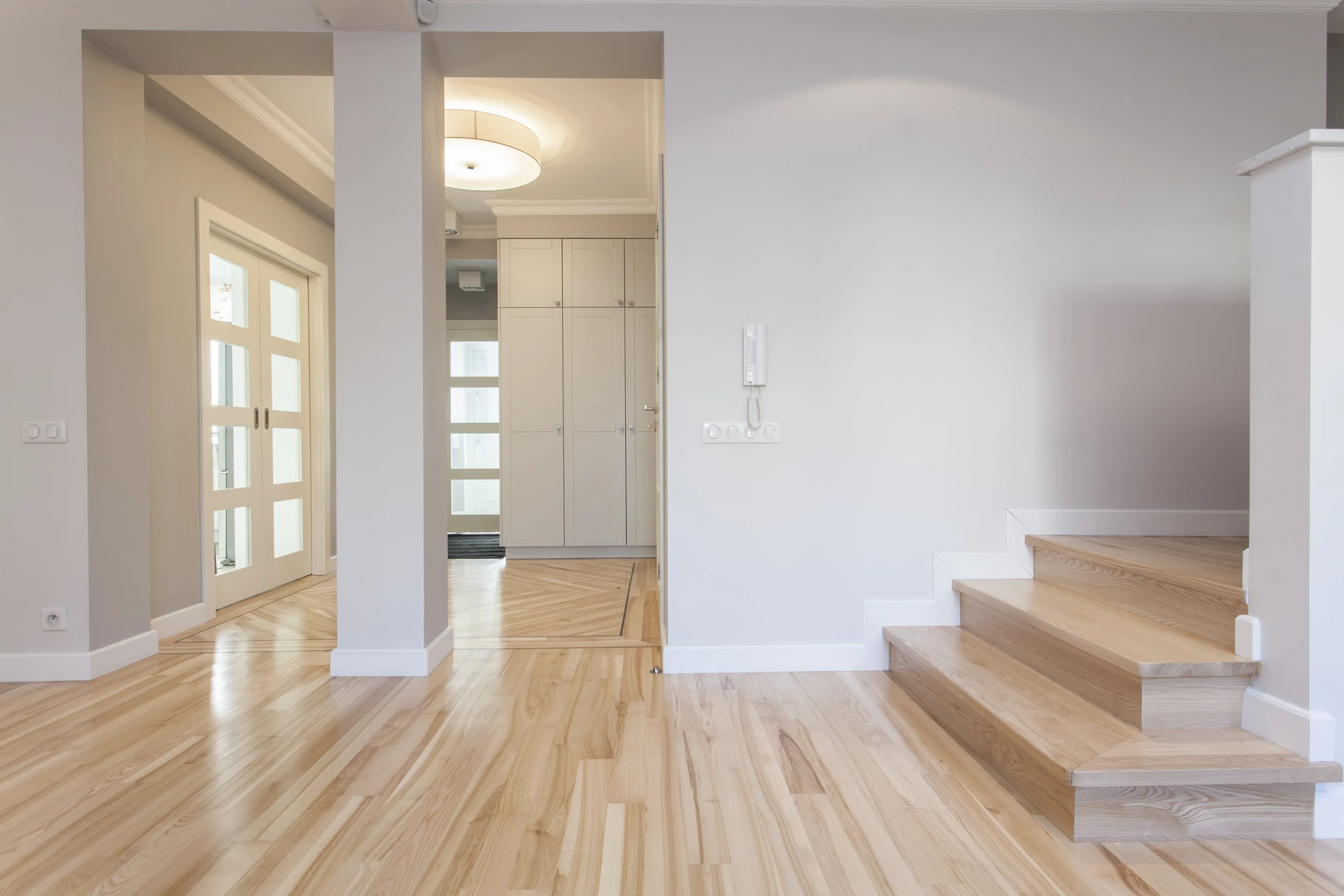 Intérieur moderne minimaliste avec canapé gris clair, suspension blanche et bois au plafond, plante verte dans cache-pot sur support métallique cuivré